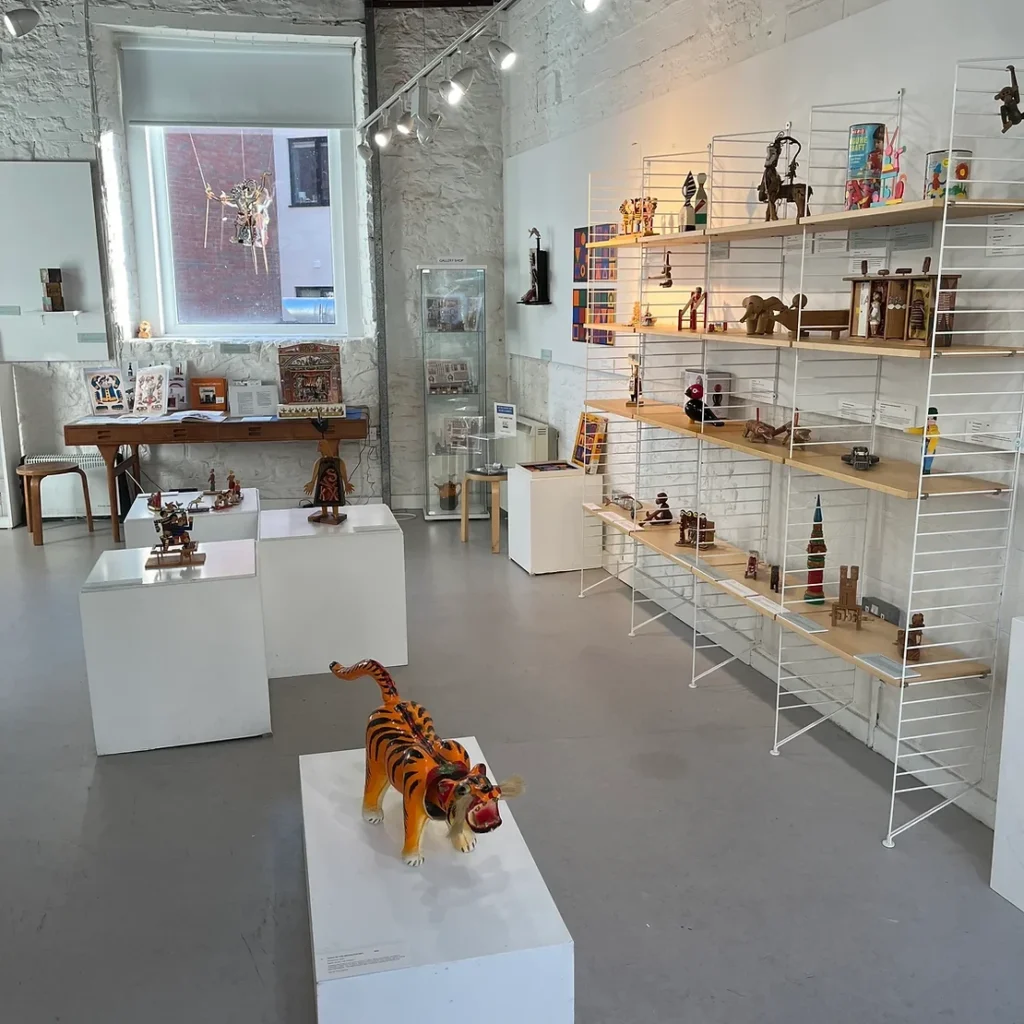 A smart, brightly lit room at The Stradling Collection in Bristol houses a display of various stylish toys, including a model tiger, a Kay Bojeson wooden monkey, and, at the far side of the room, a Neptune toy theatre on loan from Pollock's Toy Museum.