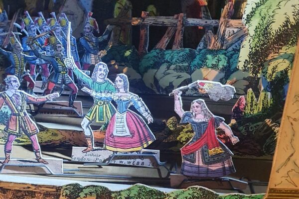 Close up of paper toy theatre characters lit by torchlight on stage