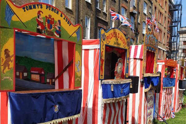 A row of brightly coloured Punch and Judy theatres set up outside in St Paul's Church garden on a sunny day