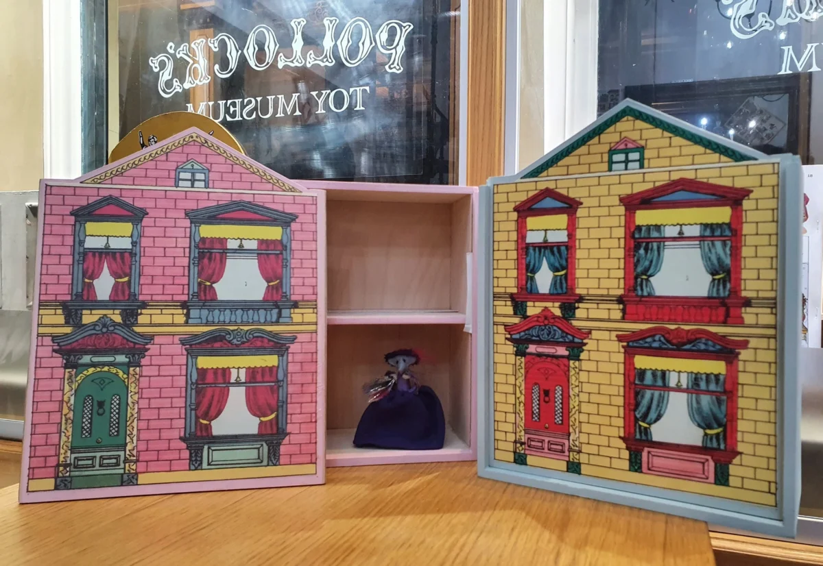 Two wooden small wooden houses with papered sliding fronts an a little toy mouse sitting inside the open house