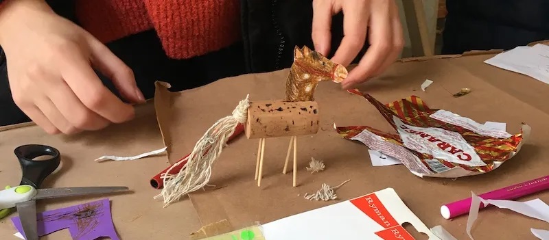 Close-up of hands making a horse from a cork, paper, string and cocktail sticks in a workshop at Pollock's Toy Museum