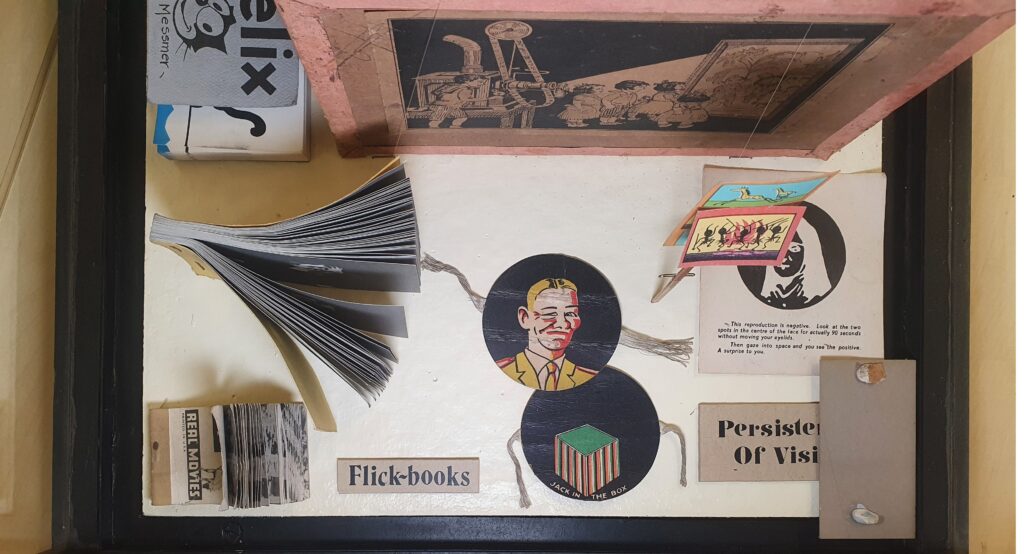 flat lay image of simple vintage paper optical toys including two flick books and two thaumatropes featuring a man's face and a green and brown box. 