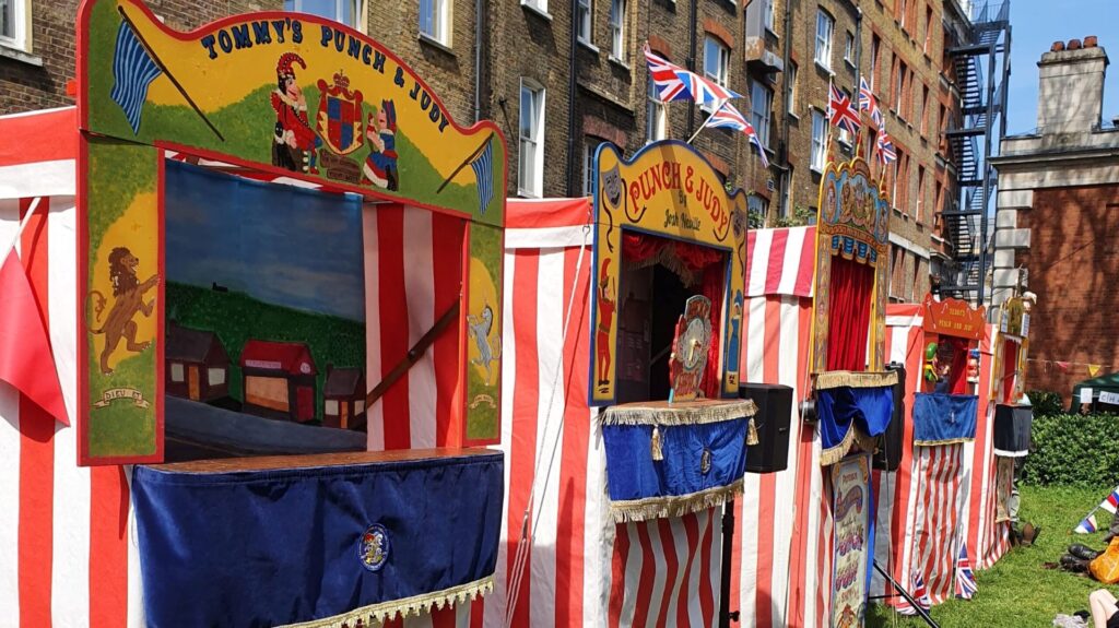 A row of brightly coloured Punch and Judy theatres set up outside in St Paul's Church garden on a sunny day