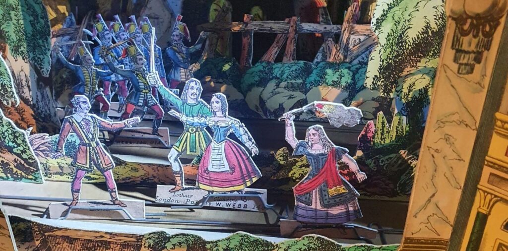 Close-up of paper toy theatre characters lit by torchlight on a stage