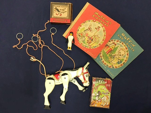 A metal Muffin the Mule puppet and other themed items lie on a dark cloth.